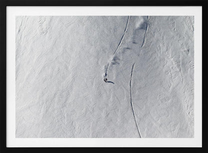 An aerial, top-down photograph of a lone snowboarder carving a turn down a vast, textured, snowy mountain slope, leaving fresh tracks in the powder. The image is presented in a simple, grey frame. Wall Art