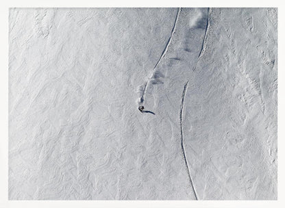 An aerial, top-down photograph of a lone snowboarder carving a turn down a vast, textured, snowy mountain slope, leaving fresh tracks in the powder. The image is presented in a simple, grey frame. Wall Art