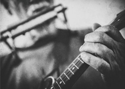 A grainy, black and white close-up photograph of a musician's hand gripping the neck of a stringed instrument. The focus is on the hand and the frets, with the musician's body and face softly blurred in the background. The image is enclosed in a silver frame. Wall Art
