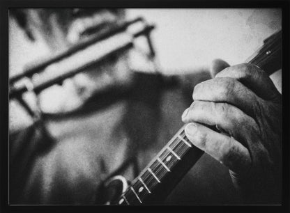 A grainy, black and white close-up photograph of a musician's hand gripping the neck of a stringed instrument. The focus is on the hand and the frets, with the musician's body and face softly blurred in the background. The image is enclosed in a silver frame. Wall Art