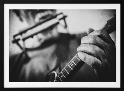 A grainy, black and white close-up photograph of a musician's hand gripping the neck of a stringed instrument. The focus is on the hand and the frets, with the musician's body and face softly blurred in the background. The image is enclosed in a silver frame. Wall Art