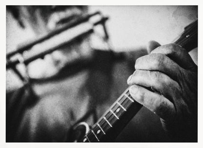 A grainy, black and white close-up photograph of a musician's hand gripping the neck of a stringed instrument. The focus is on the hand and the frets, with the musician's body and face softly blurred in the background. The image is enclosed in a silver frame. Wall Art