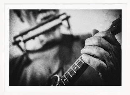 A grainy, black and white close-up photograph of a musician's hand gripping the neck of a stringed instrument. The focus is on the hand and the frets, with the musician's body and face softly blurred in the background. The image is enclosed in a silver frame. Wall Art