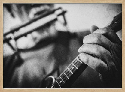A grainy, black and white close-up photograph of a musician's hand gripping the neck of a stringed instrument. The focus is on the hand and the frets, with the musician's body and face softly blurred in the background. The image is enclosed in a silver frame. Wall Art