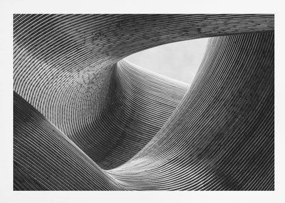 A framed, black and white abstract photograph of a swirling, textured structure. The low-angle shot looks up at curving walls made of thin, parallel lines, creating a dynamic sense of movement and depth, with an opening to a bright sky at the top. Artwork