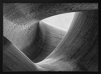 A framed, black and white abstract photograph of a swirling, textured structure. The low-angle shot looks up at curving walls made of thin, parallel lines, creating a dynamic sense of movement and depth, with an opening to a bright sky at the top. Artwork