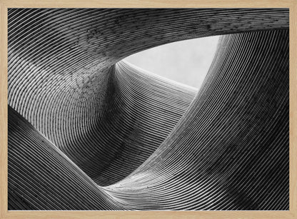 A framed, black and white abstract photograph of a swirling, textured structure. The low-angle shot looks up at curving walls made of thin, parallel lines, creating a dynamic sense of movement and depth, with an opening to a bright sky at the top. Artwork