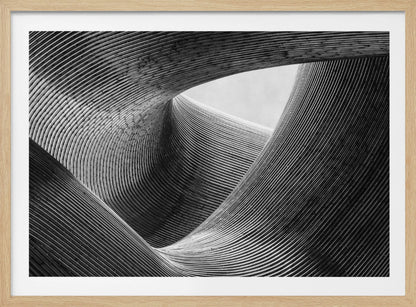 A framed, black and white abstract photograph of a swirling, textured structure. The low-angle shot looks up at curving walls made of thin, parallel lines, creating a dynamic sense of movement and depth, with an opening to a bright sky at the top. Artwork