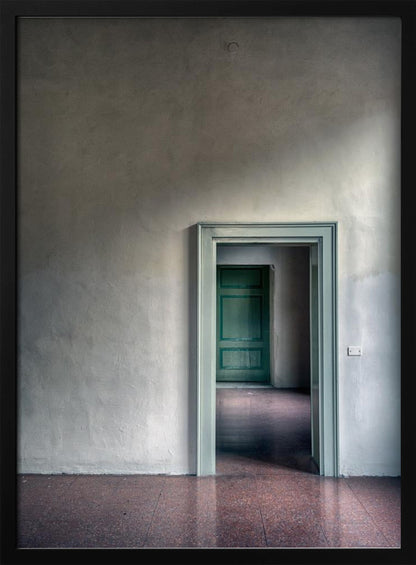 A minimalist photograph of a room with grey, textured walls and a reddish-brown floor, focusing on an open, light green doorway that reveals another room with a closed, darker green door, creating a sense of depth and perspective. Wall Art