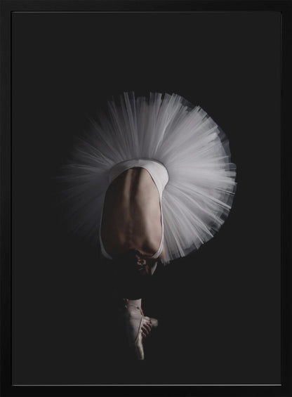 A dramatic photograph of a ballerina against a solid black background. She is bent completely forward, showing her arched back to the camera. Her white tutu fans out in a wide circle around her, and one foot in a pointe shoe is visible beneath her, balanced on its tip. Print