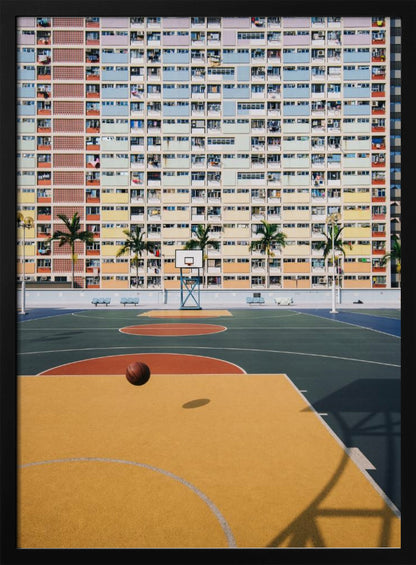 A vibrant photograph of a basketball court with a yellow and green floor, a single basketball is mid-bounce in the foreground. In the background stands the massive, symmetrical Choi Hung Estate apartment building in Hong Kong, famous for its facade of pastel rainbow colors. Palm trees line the space between the court and the building. Print