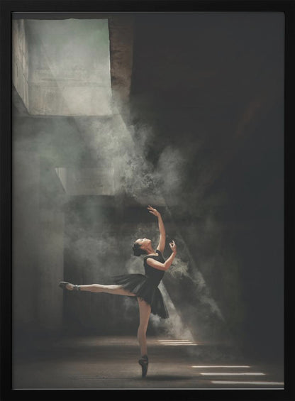 A ballerina in a black tutu gracefully performs an arabesque in a vast, dark, industrial space filled with smoke, dramatically illuminated by shafts of light from above. Poster