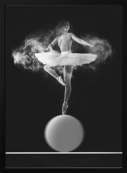 A dramatic black and white photograph of a ballerina balancing on one pointe shoe on top of a large sphere. She wears a white tutu and is surrounded by a cloud of white powder, capturing a moment of explosive, graceful movement against a solid black background. Wall Art