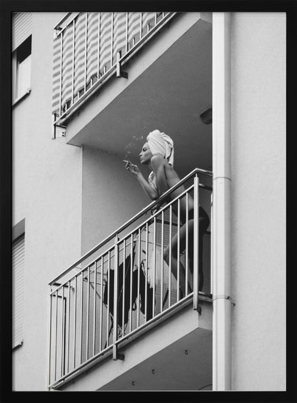 A black and white photo of a woman with a towel on her head, smoking a cigarette on an apartment balcony. The low-angle shot captures her leaning on the metal railing, with smoke drifting from the cigarette. Print