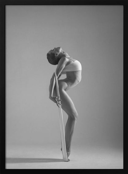 A framed black and white photograph of a graceful female dancer arching her back dramatically. She holds a long white elastic band that stretches down her body to her foot, emphasizing her athletic form and flexibility against a plain studio background. Print