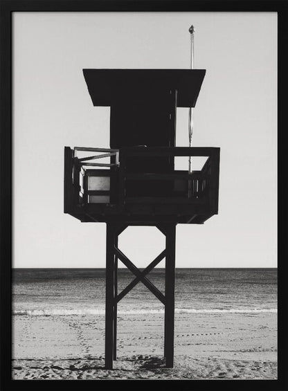 A high-contrast, black and white photograph of a silhouetted lifeguard tower standing on a sandy beach. The tower is centrally framed against a bright, empty sky, with the ocean and horizon visible in the background. Wall Art