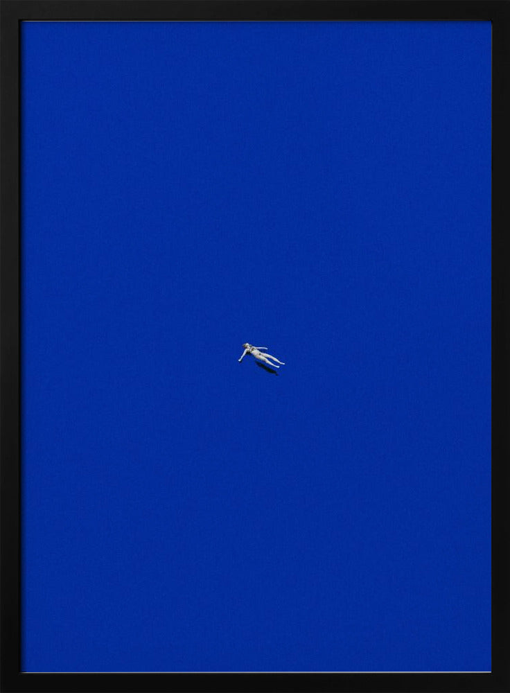 A minimalist and surreal artwork featuring a tiny, pale human figure floating peacefully in the center of an immense, solid, and vibrant blue void, all enclosed within a thin black frame. Wall Art