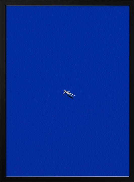 A minimalist and surreal artwork featuring a tiny, pale human figure floating peacefully in the center of an immense, solid, and vibrant blue void, all enclosed within a thin black frame. Wall Art