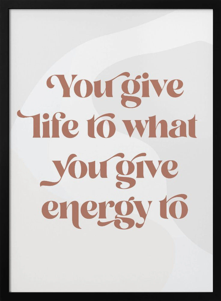 A framed motivational poster featuring the quote 'You give life to what you give energy to'. The text is printed in a dusty rose color using a stylish, retro serif font on a light gray background with subtle wavy shapes. Poster
