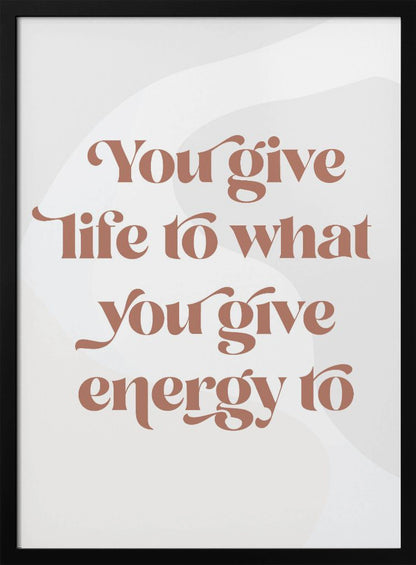 A framed motivational poster featuring the quote 'You give life to what you give energy to'. The text is printed in a dusty rose color using a stylish, retro serif font on a light gray background with subtle wavy shapes. Poster