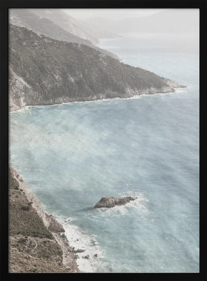 A high-angle photograph of a rugged, green coastline meeting a misty, light-blue ocean. The hazy atmosphere softens the view of the distant mountains and the waves crashing against the rocky shores. Poster