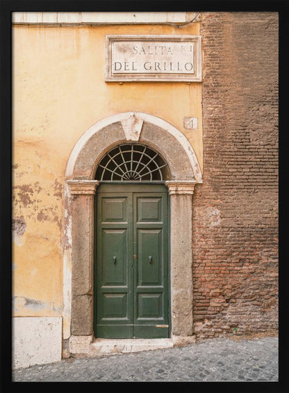 A vertical shot of a rustic European street scene featuring a dark green arched wooden door set into a stone frame. The building's facade is a mix of peeling yellow ochre plaster and exposed red brick. Above the door is a marble plaque that reads 'SALITA RI DEL GRILLO', and the ground is paved with grey cobblestones. Wall Art
