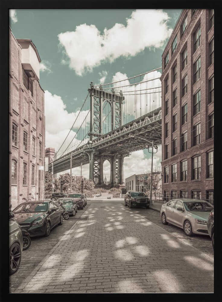 A vertical photograph of the Manhattan Bridge from a cobblestone street in DUMBO, Brooklyn, framed by tall brick buildings. The image has a vintage aesthetic with a muted teal sky and sepia-toned buildings and streets. Print