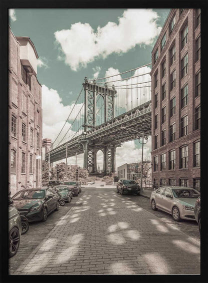 A vertical photograph of the Manhattan Bridge from a cobblestone street in DUMBO, Brooklyn, framed by tall brick buildings. The image has a vintage aesthetic with a muted teal sky and sepia-toned buildings and streets. Print