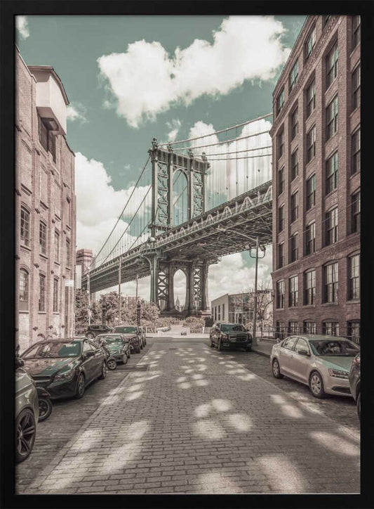 A vertical photograph of the Manhattan Bridge from a cobblestone street in DUMBO, Brooklyn, framed by tall brick buildings. The image has a vintage aesthetic with a muted teal sky and sepia-toned buildings and streets. Print