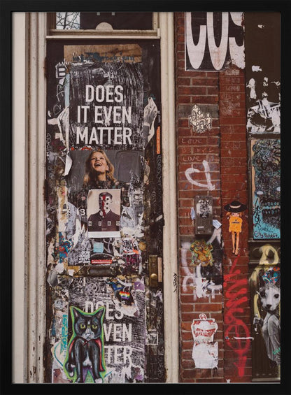 A close-up of a weathered dark door and an adjacent brick wall, both covered in a dense collage of street art, including peeling posters, stickers, and graffiti. A prominent poster on the door asks 'DOES IT EVEN MATTER' in bold white letters. Wall Art