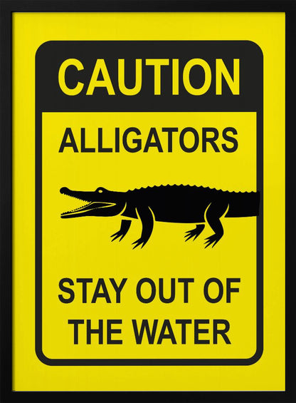 A yellow and black rectangular warning sign in a black frame. The sign reads 'CAUTION ALLIGATORS' at the top, features a black silhouette of an alligator in the center, and says 'STAY OUT OF THE WATER' at the bottom. Decor