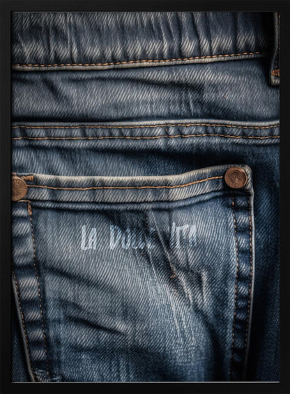 A detailed close-up photograph of a faded blue jean back pocket, showing the texture of the denim, orange stitching, and a copper rivet. Faint white text is stenciled onto the pocket. Poster