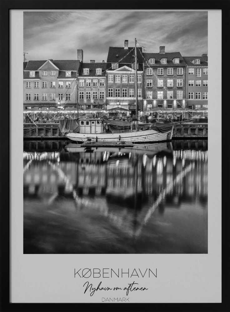 A black and white poster of Nyhavn harbor in Copenhagen at night. Historic buildings with glowing windows line the canal, and their lights create shimmering reflections in the water. A boat is docked in the foreground. The poster has text at the bottom that reads 'KØBENHAVN, Nyhavn om aftenen, DANMARK'. Poster