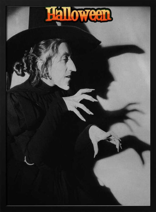 A vintage black and white poster for Halloween featuring a classic witch character. She is in profile, wearing a large pointy hat and a black gown, with long, sharp fingernails. Her menacing shadow is cast on the wall behind her, mirroring her posture. At the top of the image, the word 'Halloween' is written in a stylized orange and yellow font. Decor