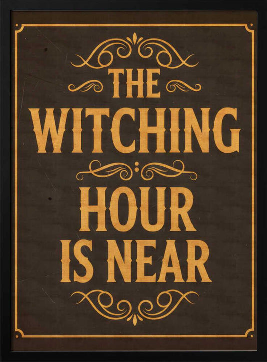 A framed vintage-style sign with a dark brown, distressed background. In a bold, golden-yellow serif font, the text reads 'THE WITCHING HOUR IS NEAR'. The text is adorned with ornate, swirling flourishes above, between, and below the lines. A thin golden-yellow border frames the entire design. Poster