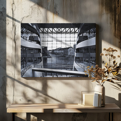 A symmetrical, black and white photograph taken from inside a modern building with curved balconies, looking out through a massive glass wall onto a canal and historic buildings on the opposite bank. A pedestrian bridge crosses the lower part of the frame. Decor