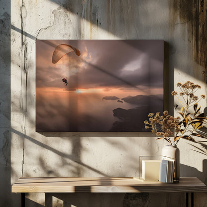 A scenic aerial view of a person paragliding over the ocean during a dramatic sunset. The orange and white parachute is in the upper left corner against a cloudy sky. The sun on the horizon casts a warm glow on the water, with silhouetted islands in the distance. Poster