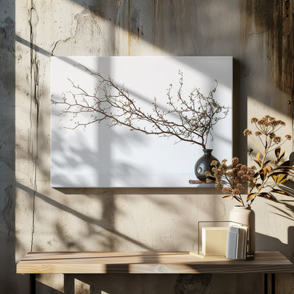 A minimalist still life of a long, delicate branch with small leaves arranged horizontally in a small, dark, round ceramic vase. The background is stark white, creating a high-contrast, serene composition, all within a silver frame. Print