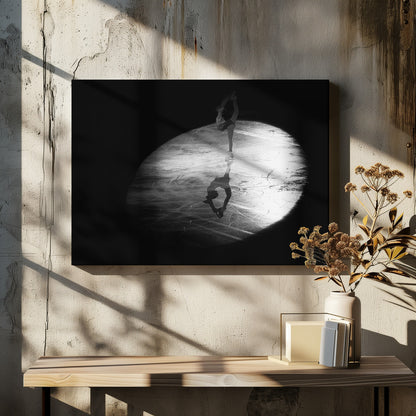 A dramatic black and white framed photograph of a female figure skater performing on ice. She is illuminated by a single spotlight, holding a graceful standing split pose, with her reflection visible on the ice below. Poster