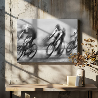A dynamic black and white action photograph of three cyclists racing, captured with a slow shutter speed to create a dramatic motion blur effect. The riders and their bikes are blurred into streaks of light and shadow, conveying a powerful sense of speed and intensity. The image is presented within a silver-toned frame. Poster
