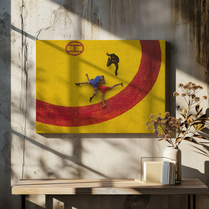 An aerial, high-angle photograph of a wrestling match in a silver frame. Two wrestlers, one in a blue singlet and the other in red, are locked in a hold on a vibrant yellow mat marked with a thick, painted red circle. A referee dressed in black stands nearby, gesturing. Artwork