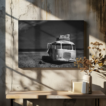 A dramatic black and white photograph of a vintage bus with luggage stacked on the roof, parked on a sandy beach. The ocean stretches out to the horizon under a dark, moody sky, with a small flock of birds flying in the distance. Print