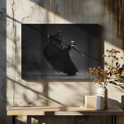 A dramatic black and white photograph of a female dancer in a flowing black gown, captured mid-motion. She is arched backwards with her head tilted up, her arms extended gracefully. The fabric of her dress billows up and around her, creating a sense of dynamic movement against a solid dark gray background. The image is presented within a silver frame. Decor