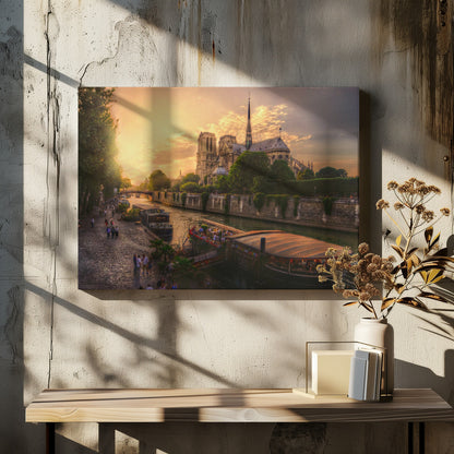 A scenic photograph of the Notre Dame Cathedral in Paris during a warm, golden sunset, as viewed from across the River Seine. People are strolling along the cobblestone riverbank and riding on tour boats docked on the water. The image is presented within a silver picture frame. Decor