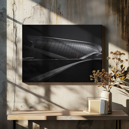 A dramatic black and white photograph of a futuristic, curved building with a dark, reflective facade. A single bright red door provides a striking pop of color. In the foreground, a light gray path curves across a dark landscape, leading the eye towards the structure. The entire image is presented within a silver-colored frame. Decor