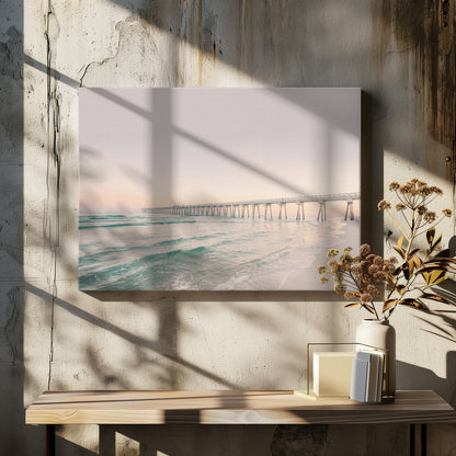 A tranquil beach scene with a long white pier extending into the turquoise ocean. The sky is a soft, pale pink, suggesting a serene sunrise or sunset, and gentle waves lap onto the sandy shore in the foreground. Poster