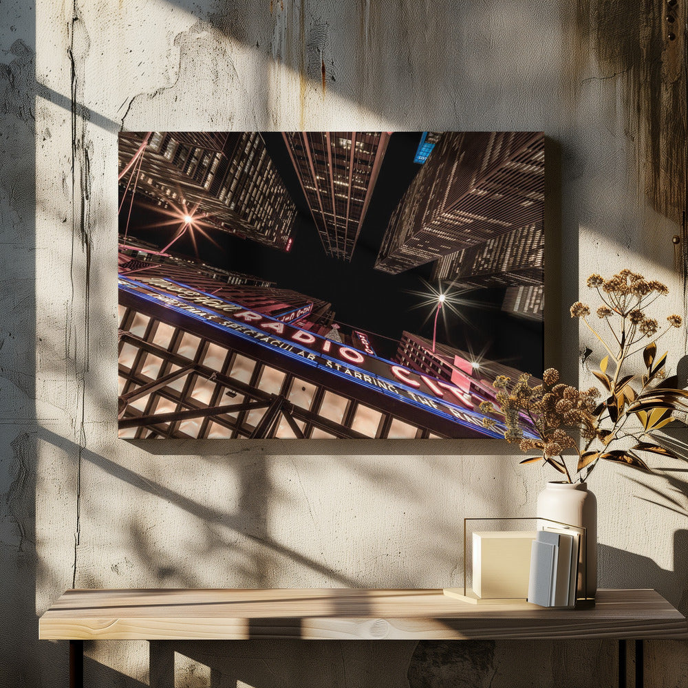A dramatic low-angle shot looking up at the iconic Radio City Music Hall marquee at night, surrounded by towering, illuminated skyscrapers against a dark sky. Decor