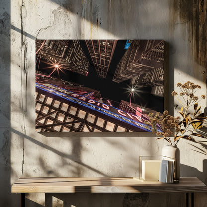 A dramatic low-angle shot looking up at the iconic Radio City Music Hall marquee at night, surrounded by towering, illuminated skyscrapers against a dark sky. Decor