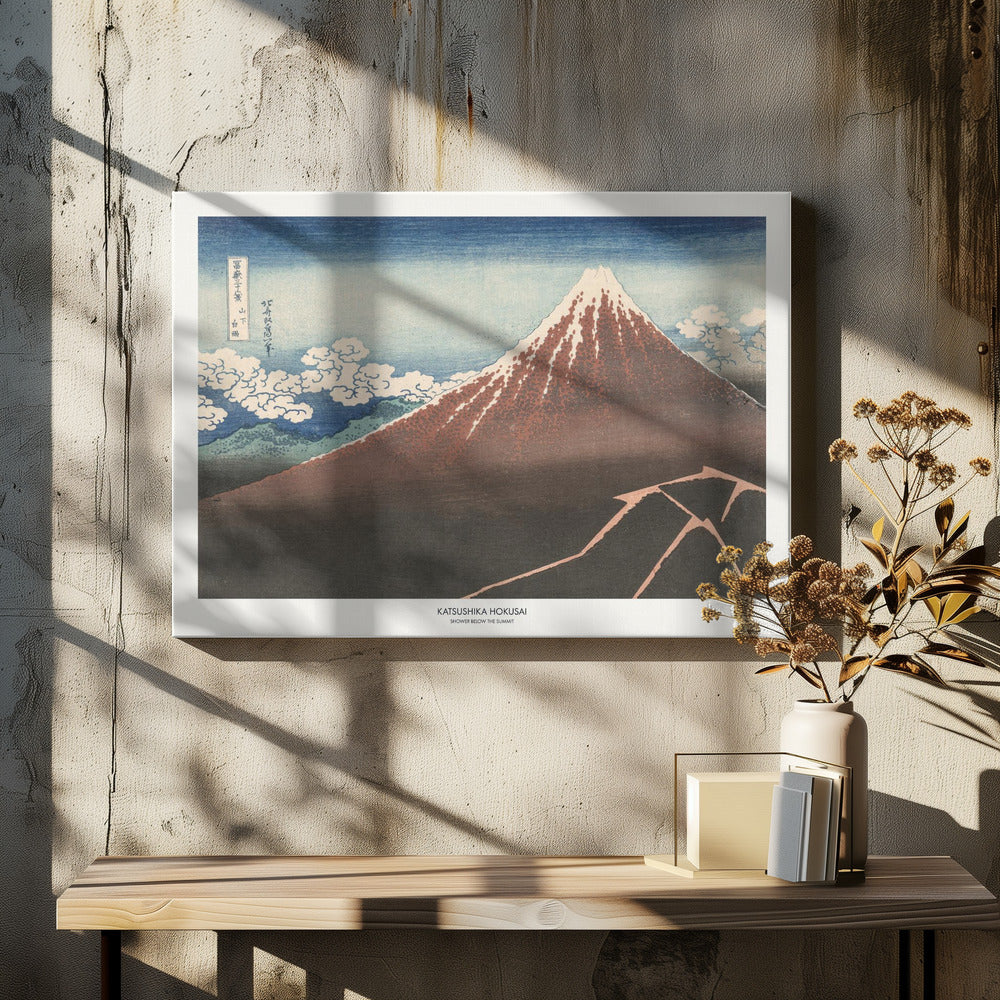 A framed Japanese woodblock print by Katsushika Hokusai titled 'Shower Below the Summit.' The print depicts a large, dark brown and reddish mountain, likely Mount Fuji, with a snow-capped peak. The sky above is a deep blue, and stylized white clouds are scattered around the mountain's slope. In the dark foreground, a jagged pink line represents a lightning strike. Artwork