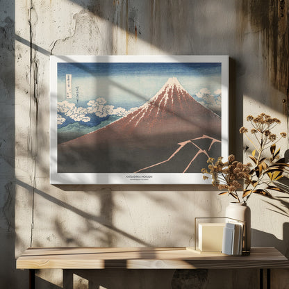 A framed Japanese woodblock print by Katsushika Hokusai titled 'Shower Below the Summit.' The print depicts a large, dark brown and reddish mountain, likely Mount Fuji, with a snow-capped peak. The sky above is a deep blue, and stylized white clouds are scattered around the mountain's slope. In the dark foreground, a jagged pink line represents a lightning strike. Artwork